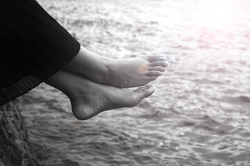 Relax bare feet on the water. Young woman sitting on sea with legs on the water with sun light...