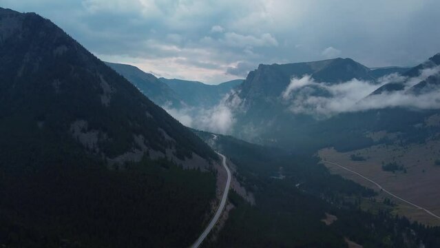 Aerial drive through misty rocky mountains on winding road
