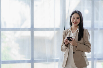 Successful Asian businesswoman using smartphone to chat with clients busy working at desk in modern office. looking at the computer screen with a smile