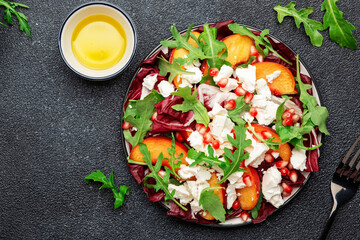 Fresh salad with arugula, radicchio, peaches, feta cheese and pomegranate seeds. Black table background, top view