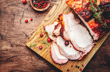 Baked pork loin, whole and cut meat pieces on rustic wooden cutting board with spices, herbs and...