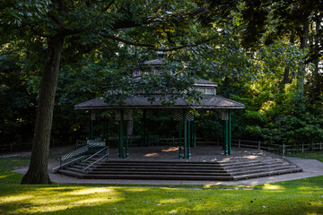 Empty music gazebo in the park - old style summer scene in the shade with sunbeam, trees and green...