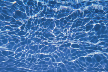 Defocus blurred transparent blue colored clear calm water surface texture with splash, bubble. Shining blue water ripple background. Surface of water in swimming pool. Blue bubble water shining.