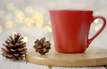 Red mug with pine cones against white bokeh orb background