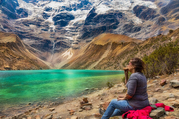 A woman sits alone at the Laguna Humantay in Peru and does eat a bun..