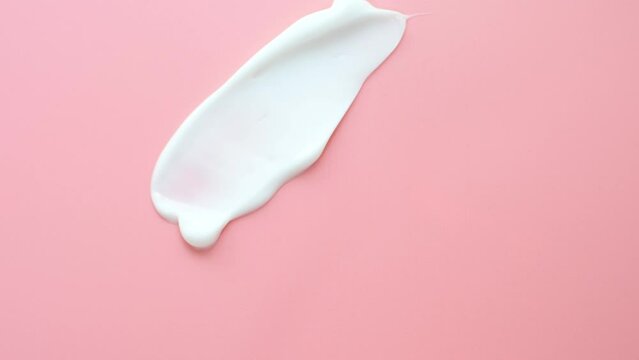 Female hand makes a smear of a moisturizing face cream using a plastic spatula on pink background.