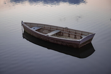 Rustic Empty Boat Floating On The Water. Pink Boat At Sunset In The Pond With Ripples and Reflections Visible On The Surface Of The Water.