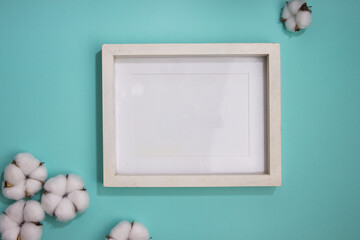 White photo frame with cotton flowers over the mint background. 
