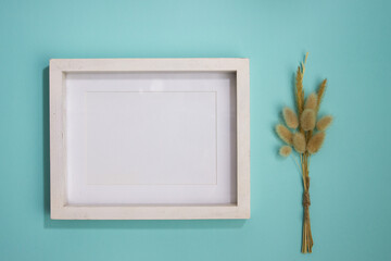 A blank white wooden frame with natural flowers over the mint background. 