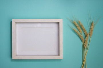 White wooden frame with natural wheat over the green table. 