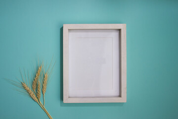 A white wooden frame with natural wheat over the mint background. 