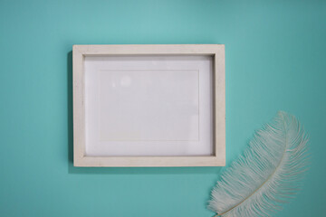 White wooden frame with white feather on mint background. 