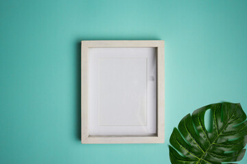 White wooden frame with green leave over the mint background. 