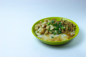 Bubur ayam Bandung or Chicken Porridge, Indonesian traditional food consist of white rice porridge, shredded chicken, cakwe, fried soybean, crackers, leek and egg. Selective focus.