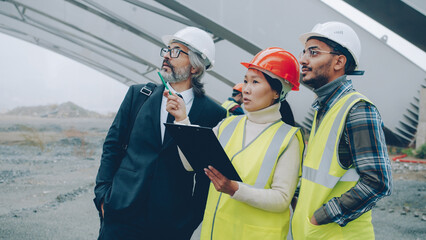 Multiracial group of workers are talking to construction inspector looking at blueprints in building area. Projects and people concept. - 536888790