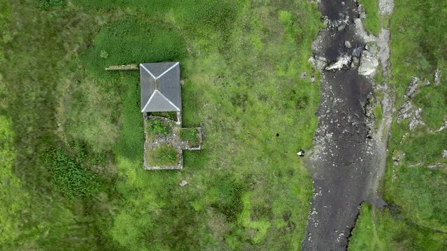 Aerial drone footage flying high above Gameshope bothy (a remote mountain shelter), looking directly down on grass and hikers with a dog by a river as they explore their surroundings, Scotland