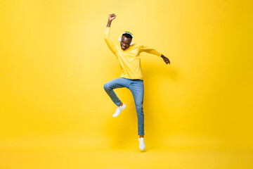 Fototapeta na wymiar Ecstatic young African man wearing headphones listening to music and dancing with hand up in studio yellow color isolated background