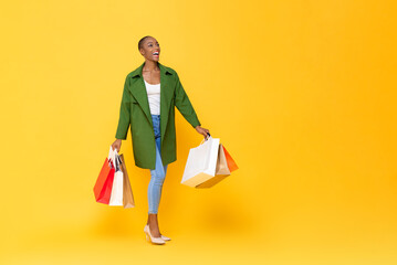 Trendy fashionable African American woman carrying colorful shopping bags walking on yellow color...