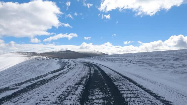 Viajando por un camino de tierra ripio con nieve. Se ven el cielo azul y nubes. Imagen desde el techo de una camioneta con una cámara de acción