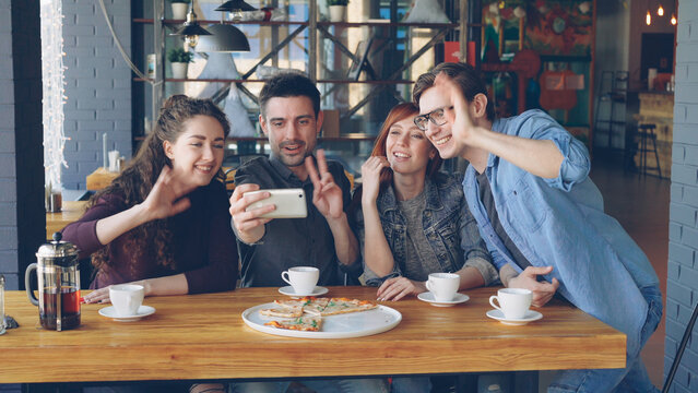 Young people are having funny video chat holding smartphone looking at webcam chatting to friend at table inside nice cafe. Modern communication and friendship concept.