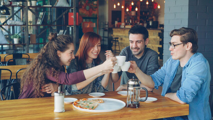 Happy friends are celebrating reunion in cafe over drinks and pizza, clanging cups, drinking and sharing news. Friendship, modern lifestyle, communication and celebration concept.