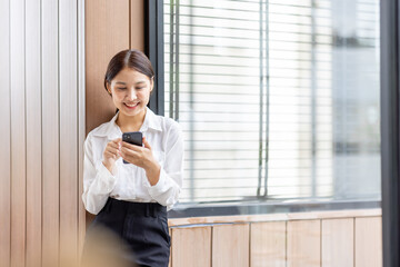 Fototapeta premium Happy millennial hispanic teen girl checking social media holding smartphone at home. Smiling young asian woman using mobile phone app playing game, shopping online, ordering delivery relax on desk.