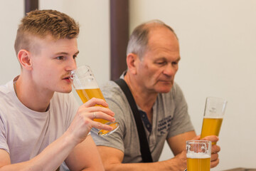 Two men adult son and senior father drinking light beer, cheering together and having a discussion...