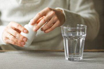 Close-up man's hands holds white plastic bottle with pills and ready to take supplement pill with glass of water.