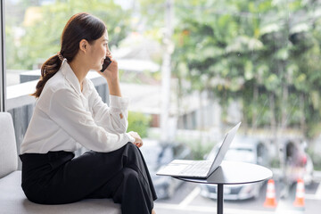 Asian businesswoman talking on phone, using laptop, looking at screen, entrepreneur manager consulting client by call, looking at computer screen, discussing project, reading information