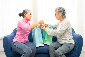 Fototapeta premium Two happy senior women exchange gifts and talking. senior ladies at home in sofa exchange present for holiday or birthday.Real life of elderly woman