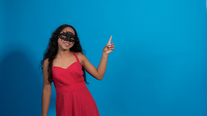 Fototapeta premium Niña con vestido rojo en fondo azul, haciendo poses con antifaz.