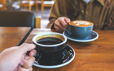 Closeup image of a couple people holding and drinking coffee together in cafe