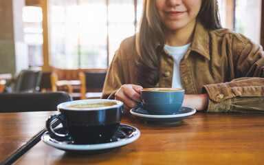 Closeup image of a young woman holding and drinking coffee with friend in cafe