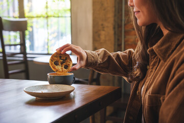 Closeup image of a young woman dipping a cookie into hot drinks