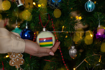 Close up of girls hand holding a Christmas ball for a fir tree with the flag of Mauritius. New year...