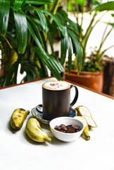 Banana chocolate latte with fresh banana and chocolate drops on white table