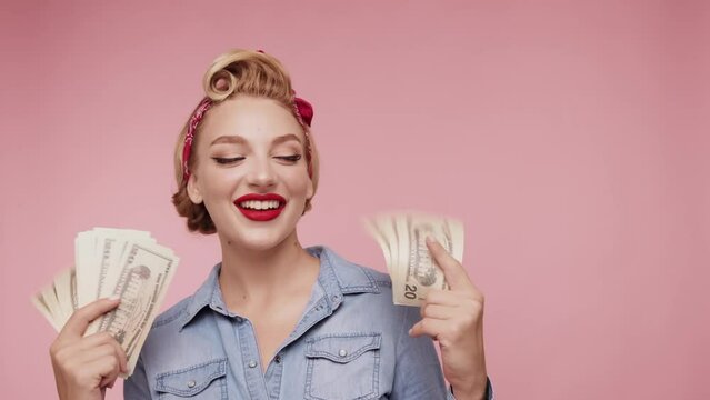 Beautiful blond woman with cash dollars in hands. Caucasian girl hold fan of cash money in dollars banknotes. Girl posing isolated on pink background studio with cash. Pop-art style.