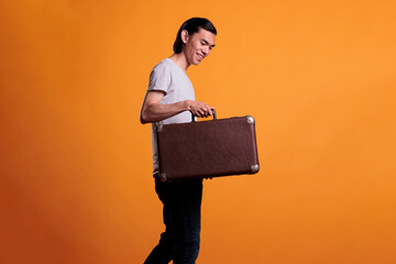 Happy young asian traveler holding suitcase, traveling, tourism concept. Cheerful smiling man standing with baggage, tourist walking with luggage, going on vacation, journey