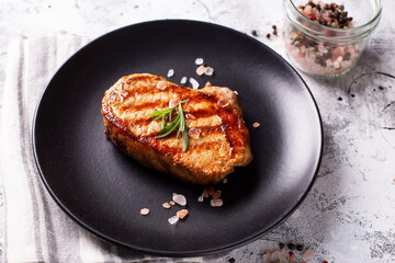 Grilled delicious beef steak with spices and rosemary on black plate on grey textured background. Top view.