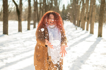Fat caucasian woman playing snowballs in the park. 