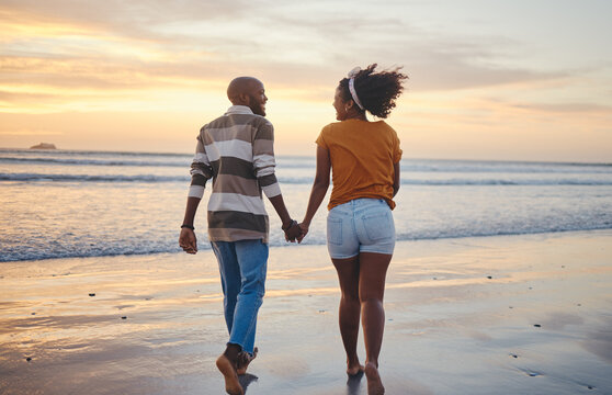 Black Couple, Holding Hands And On Beach With Sunset For Romance, Celebrate Relationship Or Holiday Together. Love, Happy Man And Woman Bare Feet, Relax Or Smile On Romantic Seaside Vacation Or Break