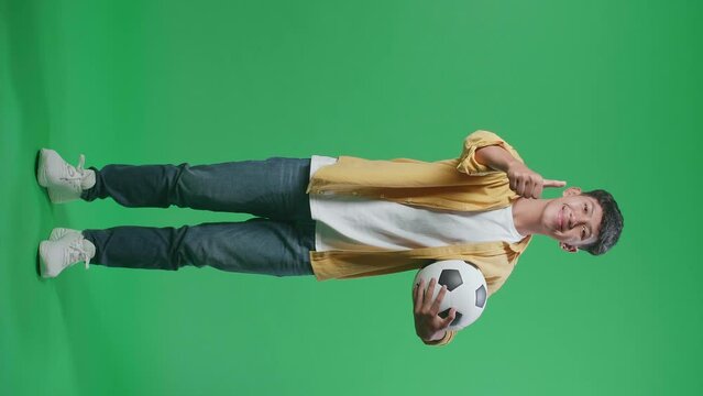 Full Body Of Asian Boy With A Ball Showing Thumbs Up Gesture While Cheering Soccer On Green Screen Background

