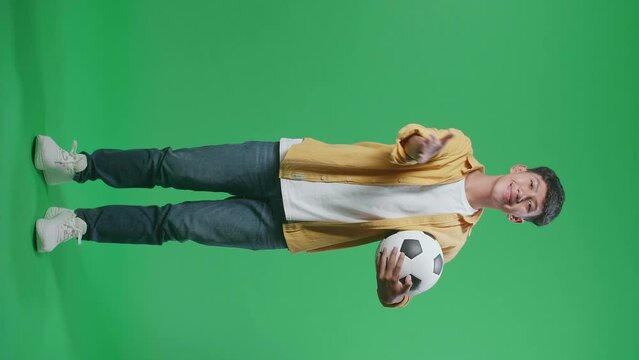 Full Body Of Asian Boy With A Ball Blowing Kisses And Smiling To Camera While Cheering Soccer On Green Screen Background
