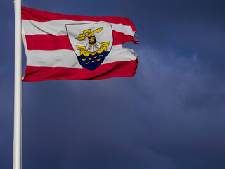 Galway county flag with sign Galway in Irish language and emblem, cloudy sky background. Ireland. Popular travel and tourism area. Copy space for message.