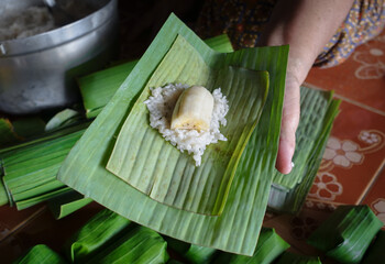 Elderly woman hands wrapped cooking Thai traditional dessert steamed sticky rice with banana ,Khao...