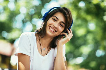 Young woman is listening to music using headphones in the park