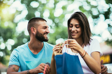 Coffee break after shopping. Couple in love drinking coffee in the cafe and sharing new purchases with each other.