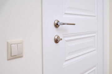 A white door with a lock in the home room and a light switch. Metal door handle and plastic light switch in the apartment