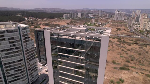vista a&eacute;rea desde dron rodeando un edificio con ventanas espejadas, se ven muchos edificios de oficinas y el oc&eacute;ano de fondo