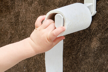 Toddler baby reaches for toilet paper, child s hand with hygiene products close-up. White toilet...